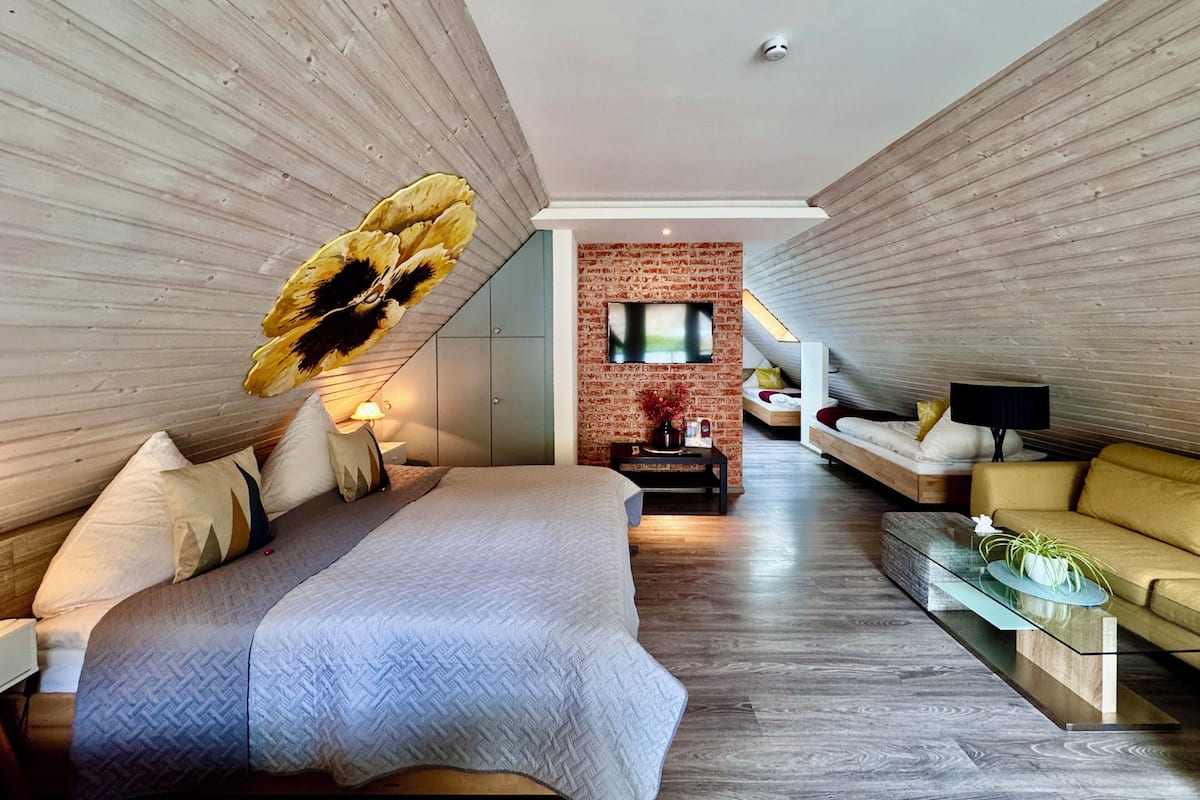 Un dormitorio moderno con una cama grande, un televisor fijado a una pared de ladrillo y un sofá.