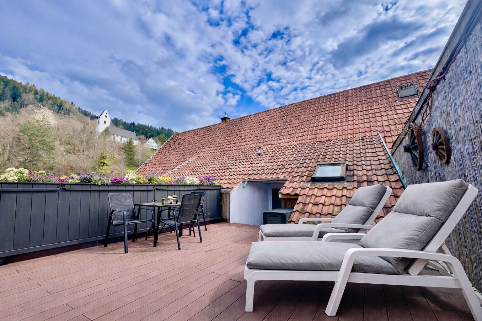 En overdækket terrasse med udendørs møbler, en træterrasse og en bygning med tegltag.
