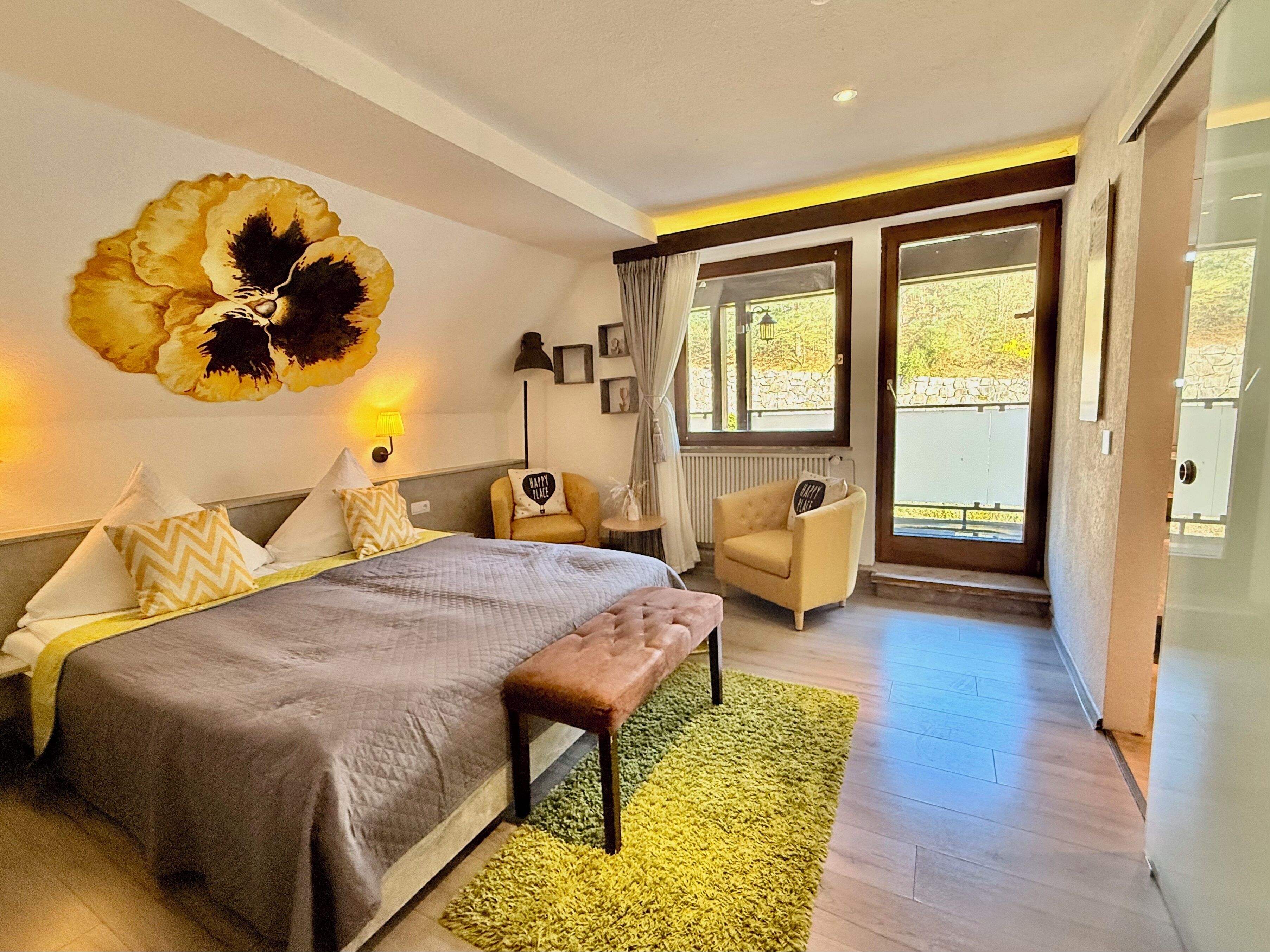 A modern bedroom with a bed, bedside lamp, chair, and a large flower artwork on the wall.