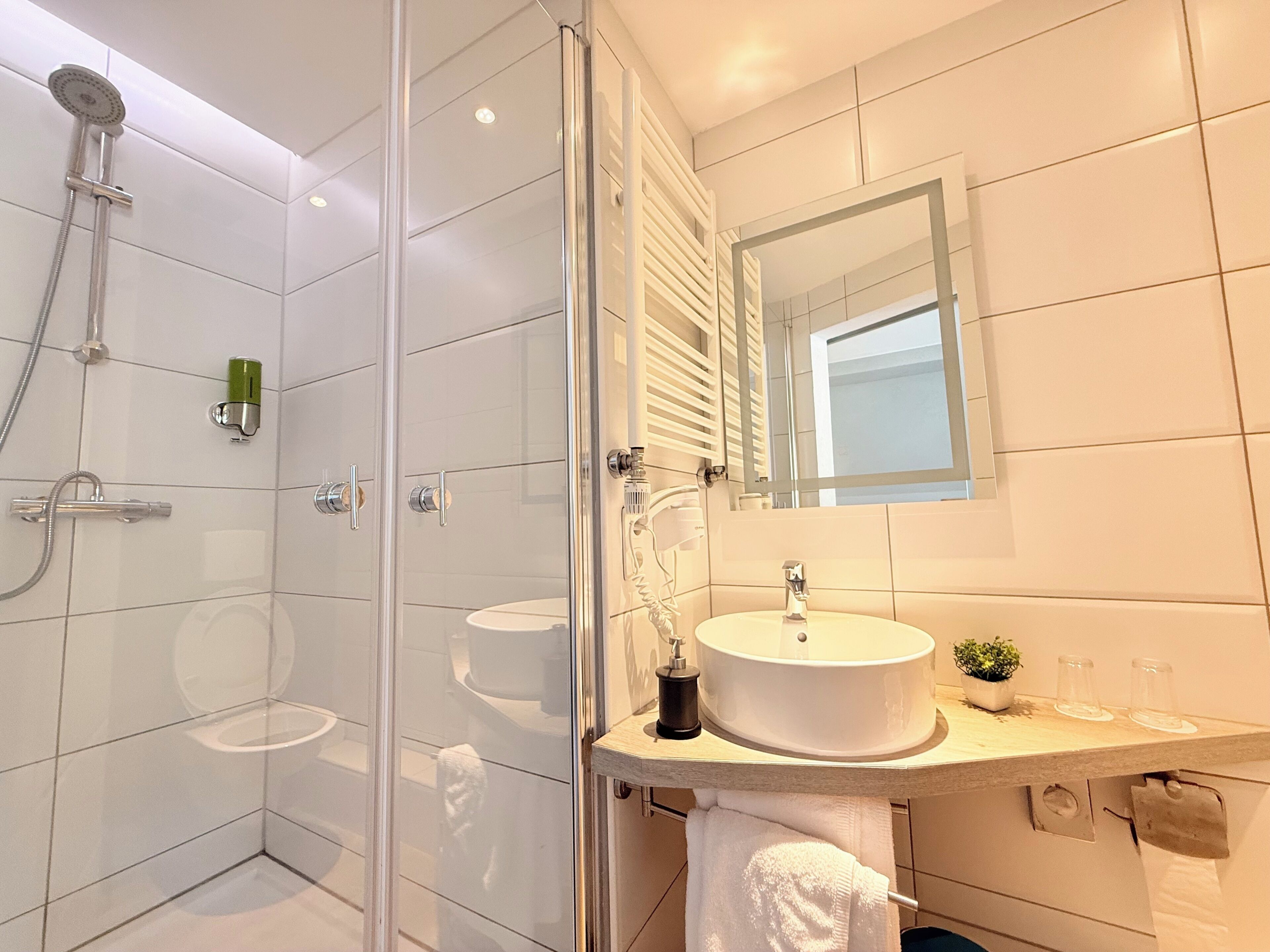 A modern bathroom with a glass-enclosed shower, a white sink, and a mirror above the countertop.