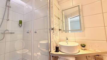 A modern bathroom with a glass-enclosed shower, a white sink, and a mirror above the countertop.