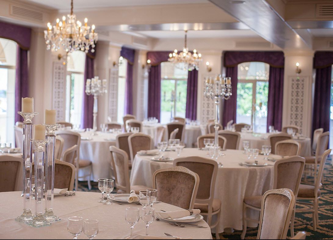A banquet hall with round tables, chairs, and chandeliers.