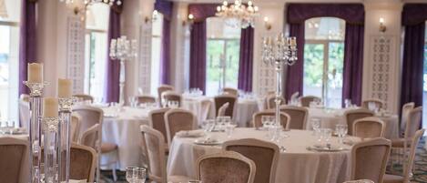 A banquet hall with round tables, chairs, and chandeliers.