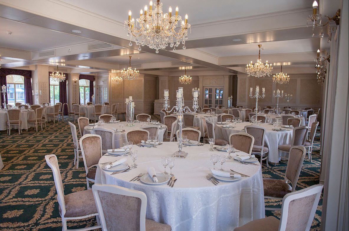 A banquet hall with round tables, white tablecloths, and chandeliers.