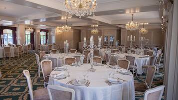 A banquet hall with round tables, white tablecloths, and chandeliers.