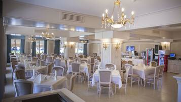 A spacious dining area with multiple tables and chairs, a chandelier, and a Coca-Cola vending machine.