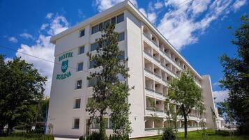 Un immeuble d’hôtel à plusieurs étages, doté de balcons, avec un ciel dégagé et entouré de verdure.