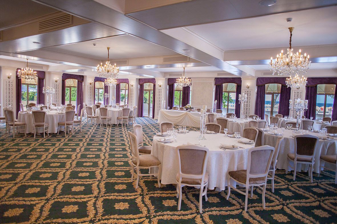 A banquet hall with round tables, chairs, chandeliers, and a patterned carpet.