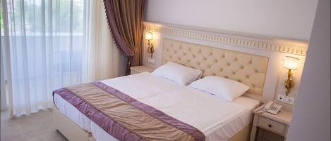 A hotel room with a large bed, two bedside tables, an air conditioner, and a window with curtains.