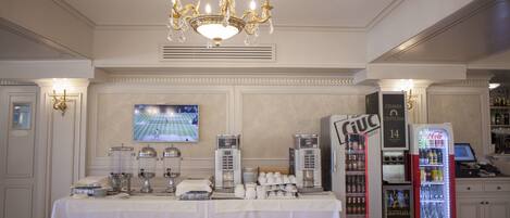 Una habitación de hotel con una mesa de comedor preparada para el desayuno, un minibar, un televisor y un dispensador de Coca-Cola.