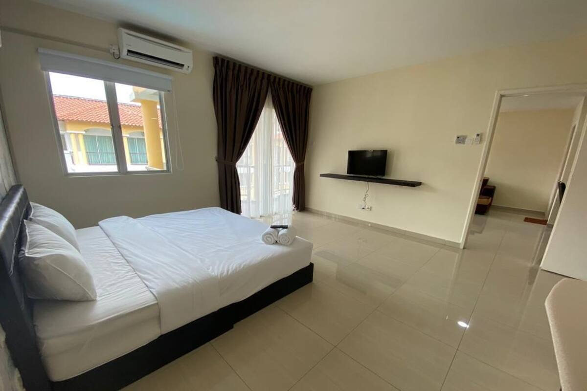 A hotel room with a bed, a TV on a shelf, a window with curtains, and a door leading to another room.