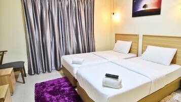 Habitación de hotel con dos camas, un escritorio, una silla, un tapete morado y un cuadro de un árbol en la pared.