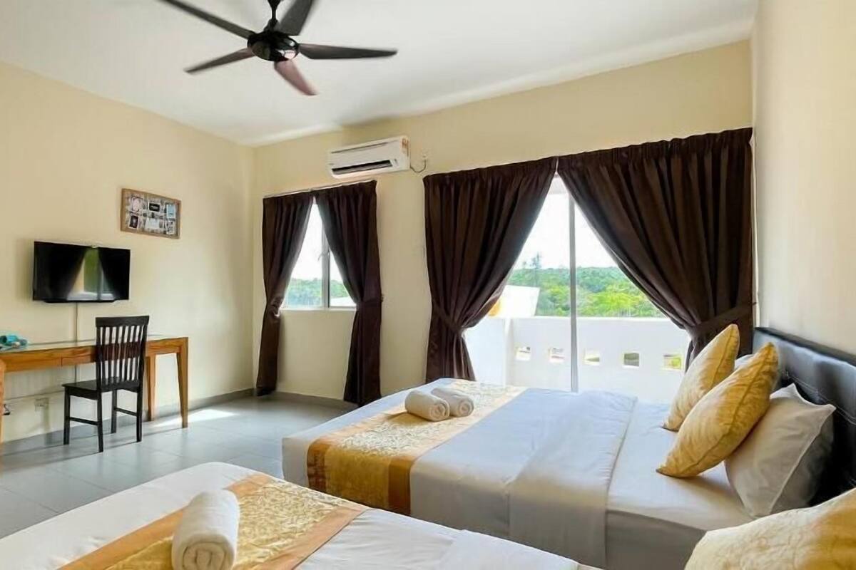 A hotel room with two beds, a desk, a TV, and an air conditioning unit.