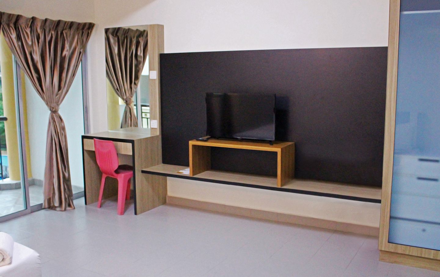 Una camera moderna con una scrivania, una sedia, una televisione su un mobile in legno e un'ampia finestra con tende.