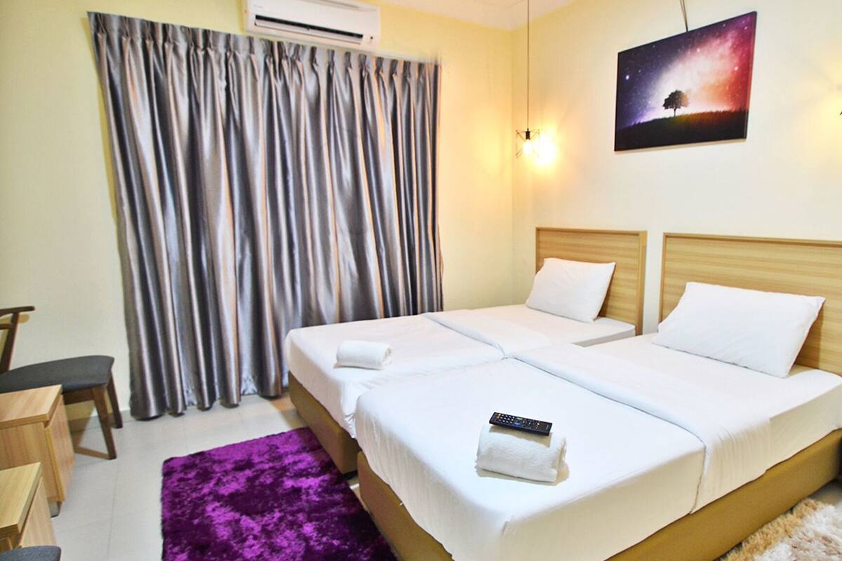 A hotel room with two beds, a desk, a chair, a purple rug, and a painting on the wall.
