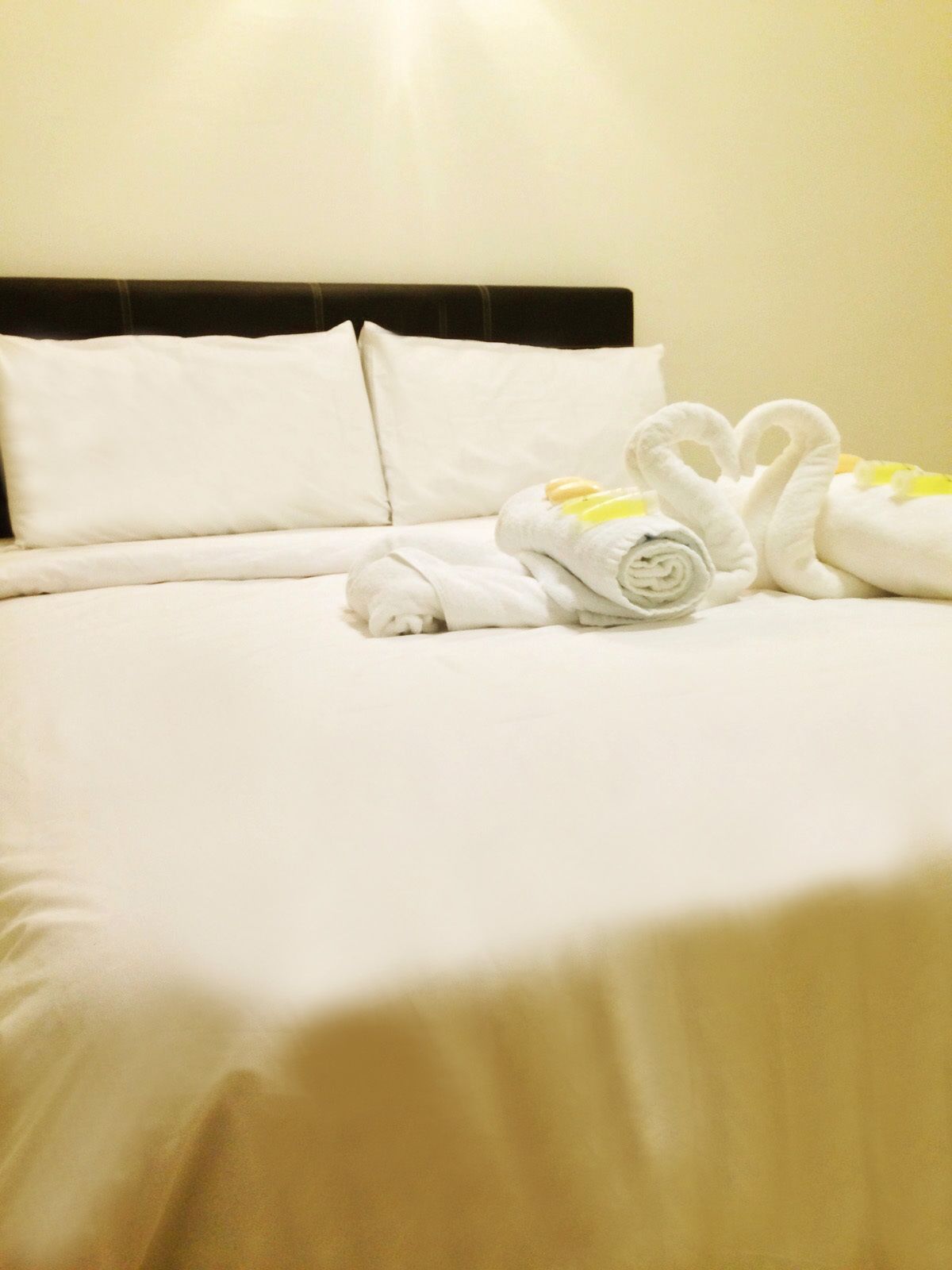 Una cama bien hecha con sábanas blancas y dos toallas dobladas en forma de cisne.
