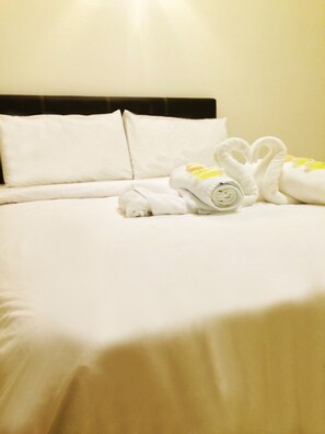 A neatly made bed with white linens and two towels folded into swans. - Tiara Desaru Residences (Bandar Penawar)