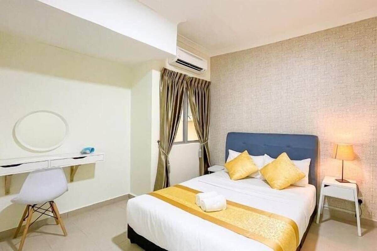 A hotel room with a bed, a desk, a chair, a lamp, and an air conditioning unit.