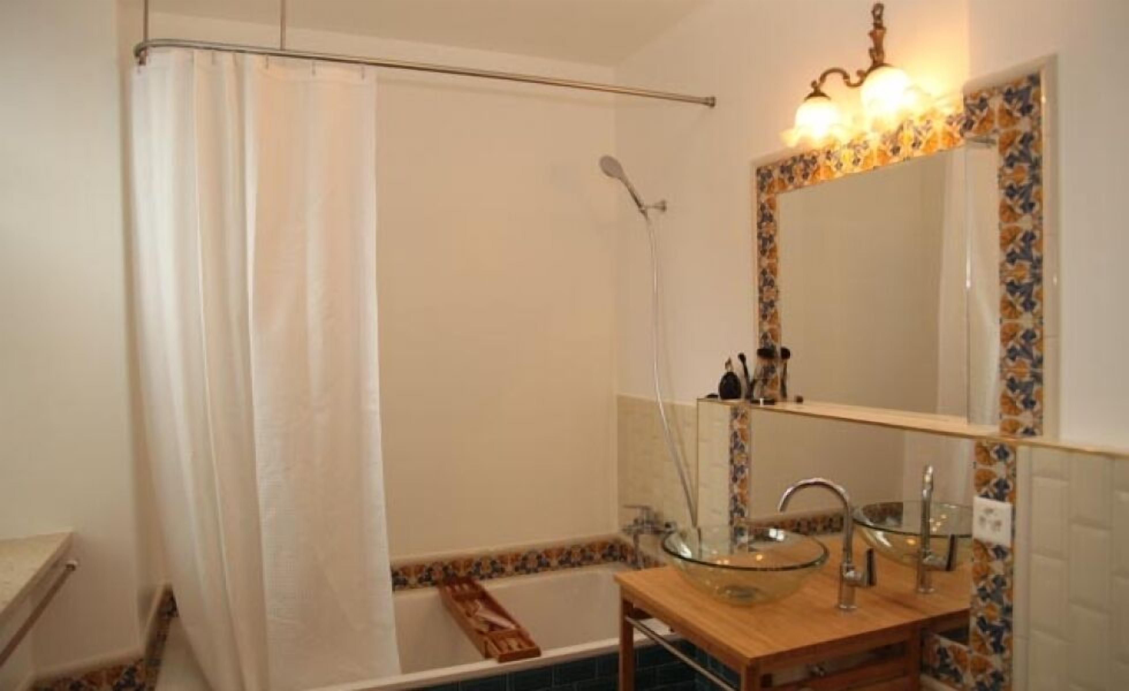 Une salle de bain avec un lavabo entouré de parois en verre, une douche avec un rideau et un miroir doté d’un cadre décoratif.