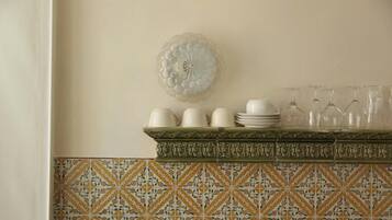 Una cocina con un salpicadero decorativo, un plato de vidrio montado en la pared y un estante con tazas, platos y copas de vino blancos.