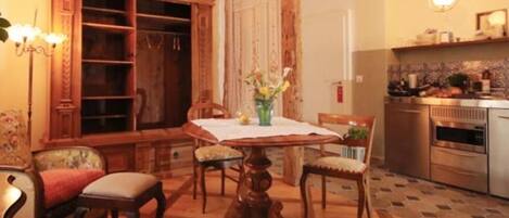 Un comedor con una mesa de madera, sillas y un florero. Hay una zona de cocina con estufa y armarios.
