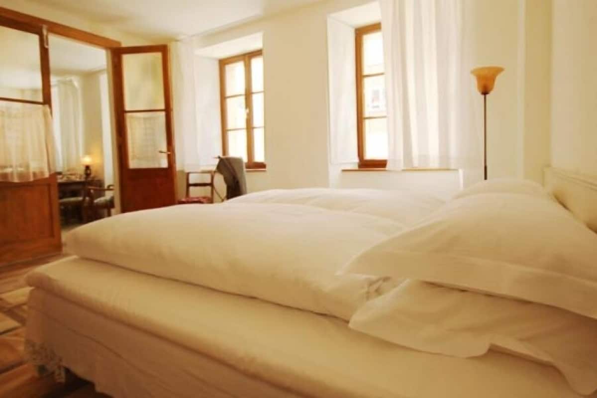 A large bed with white linens in a room with wooden furniture and a window.