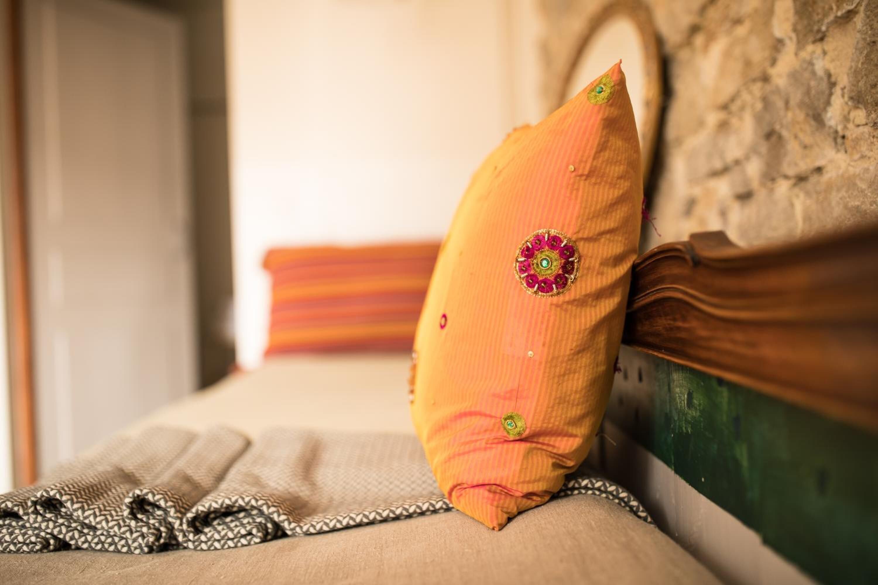 A bed with a wooden headboard, a beige blanket, and a decorative pillow with a floral pattern.