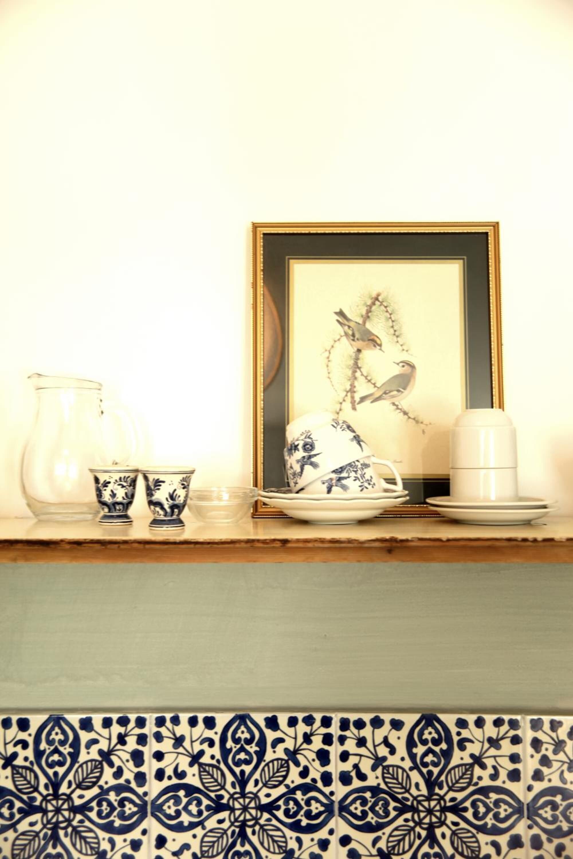 A dining table with a framed artwork, a pitcher, cups, and a teapot.