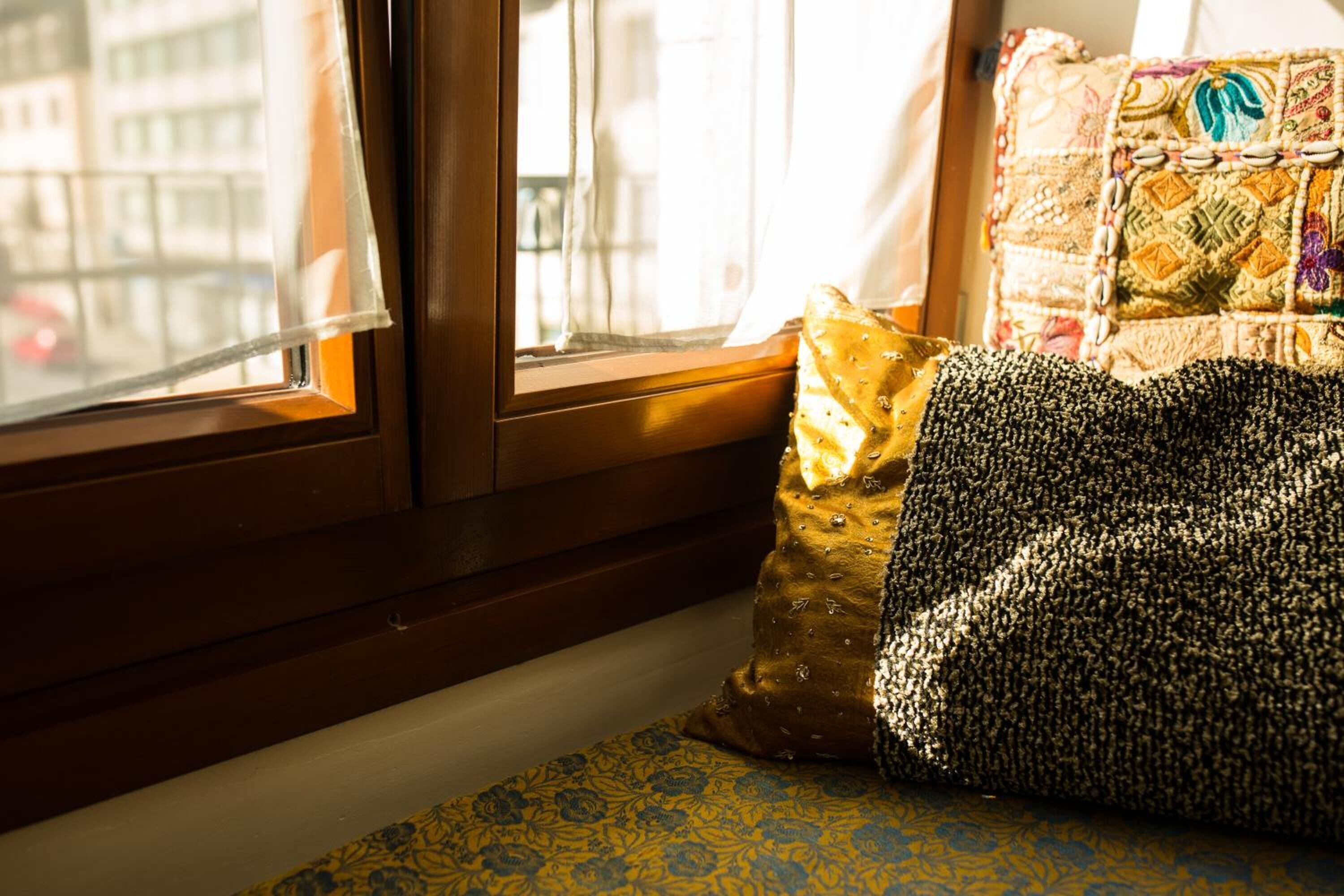 A window with a view of buildings, a patterned cushion, and a textured pillow on a window sill.