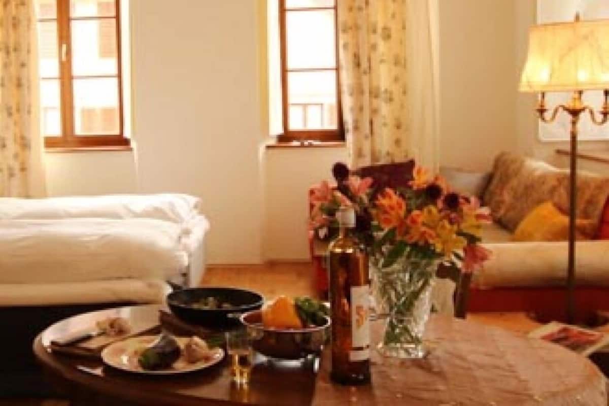 A hotel room with a bed, a dining table with plates, a vase with flowers, and a lamp.