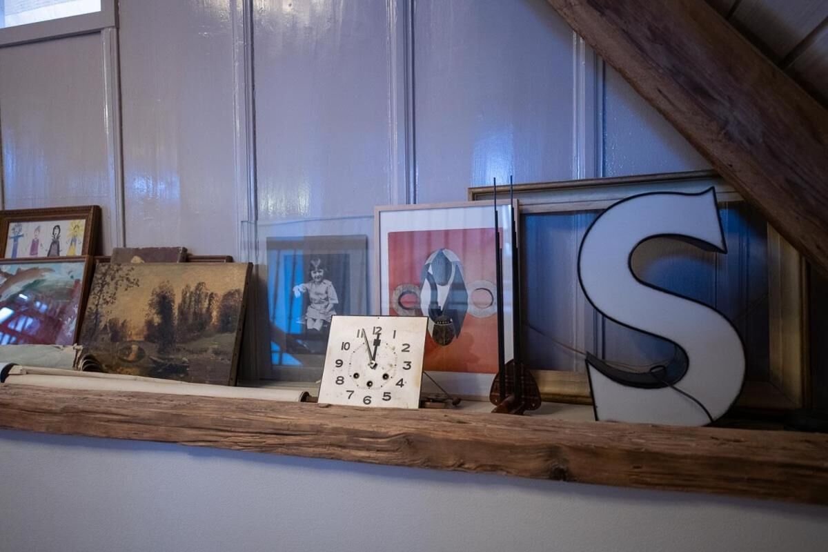 Una estantería de madera con varias obras de arte enmarcadas y un reloj.