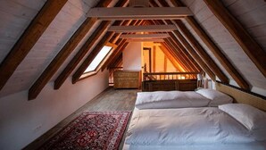A bedroom with a sloped ceiling, wooden beams, a bed, a dresser, and a rug. - Guesthouse Le Locle (Le Locle)