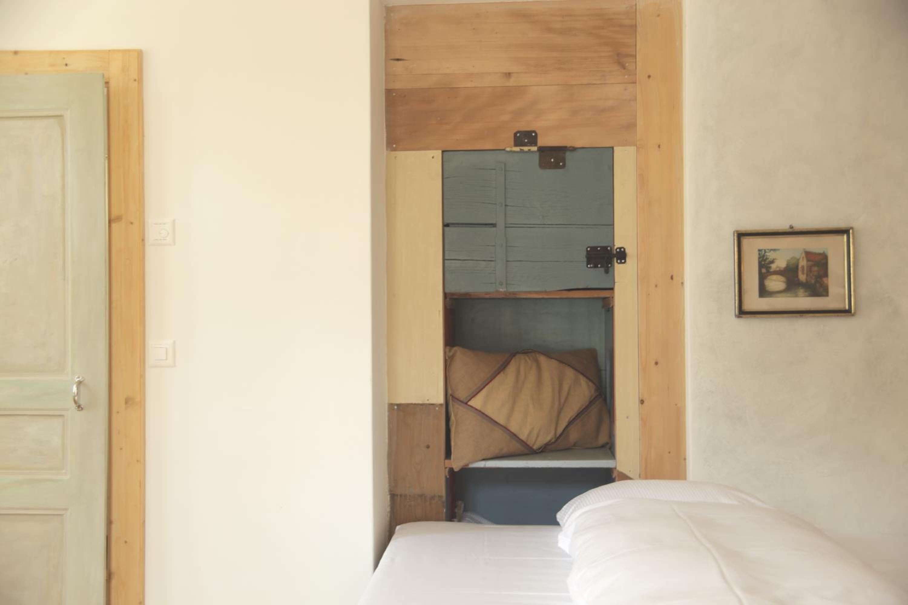 A room with a bed, a wooden door, and a blue cabinet with a brown cushion.