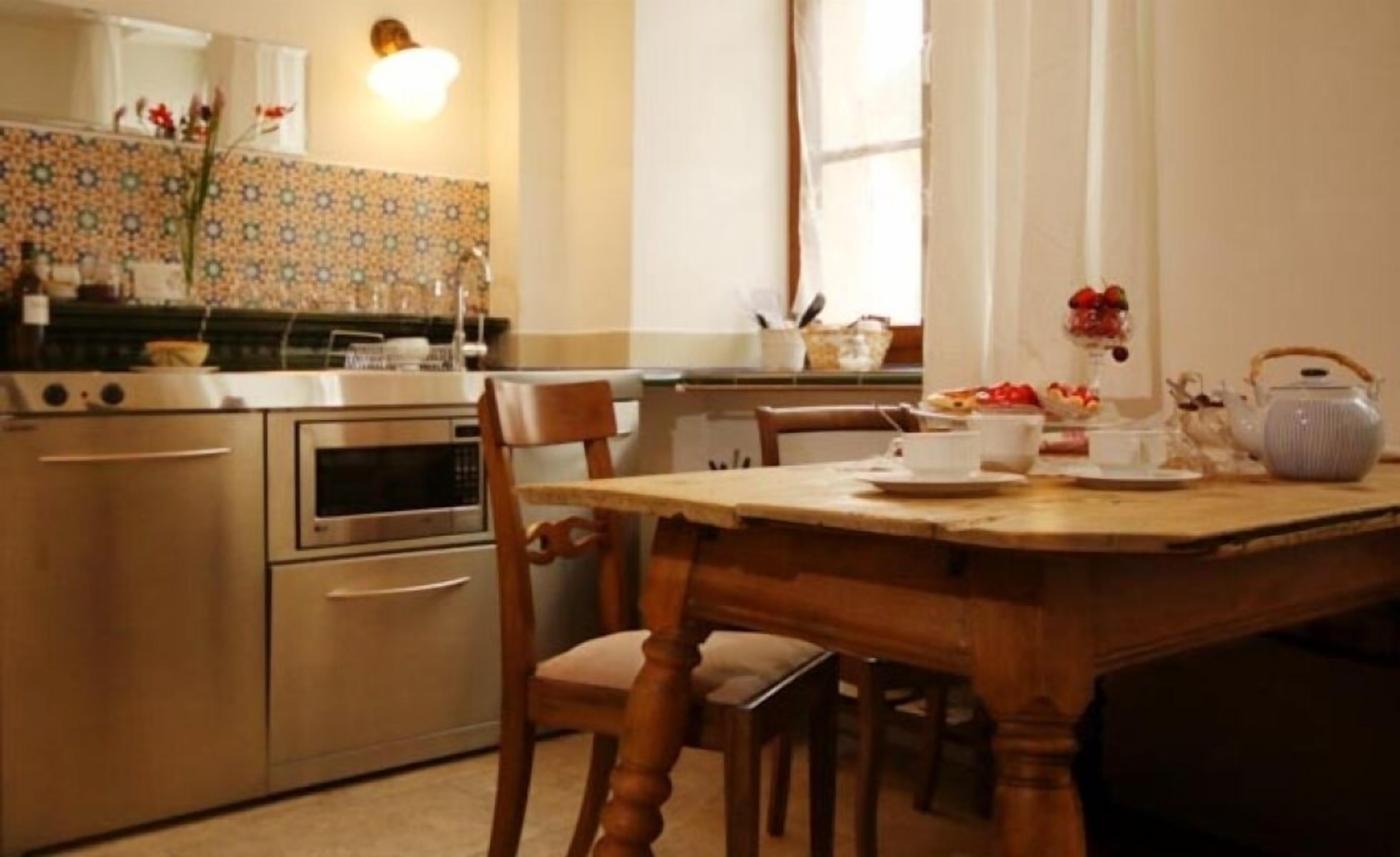 Een keuken met een fornuis, oven en magnetron. Er is een houten eettafel met stoelen en een vaas met bloemen.