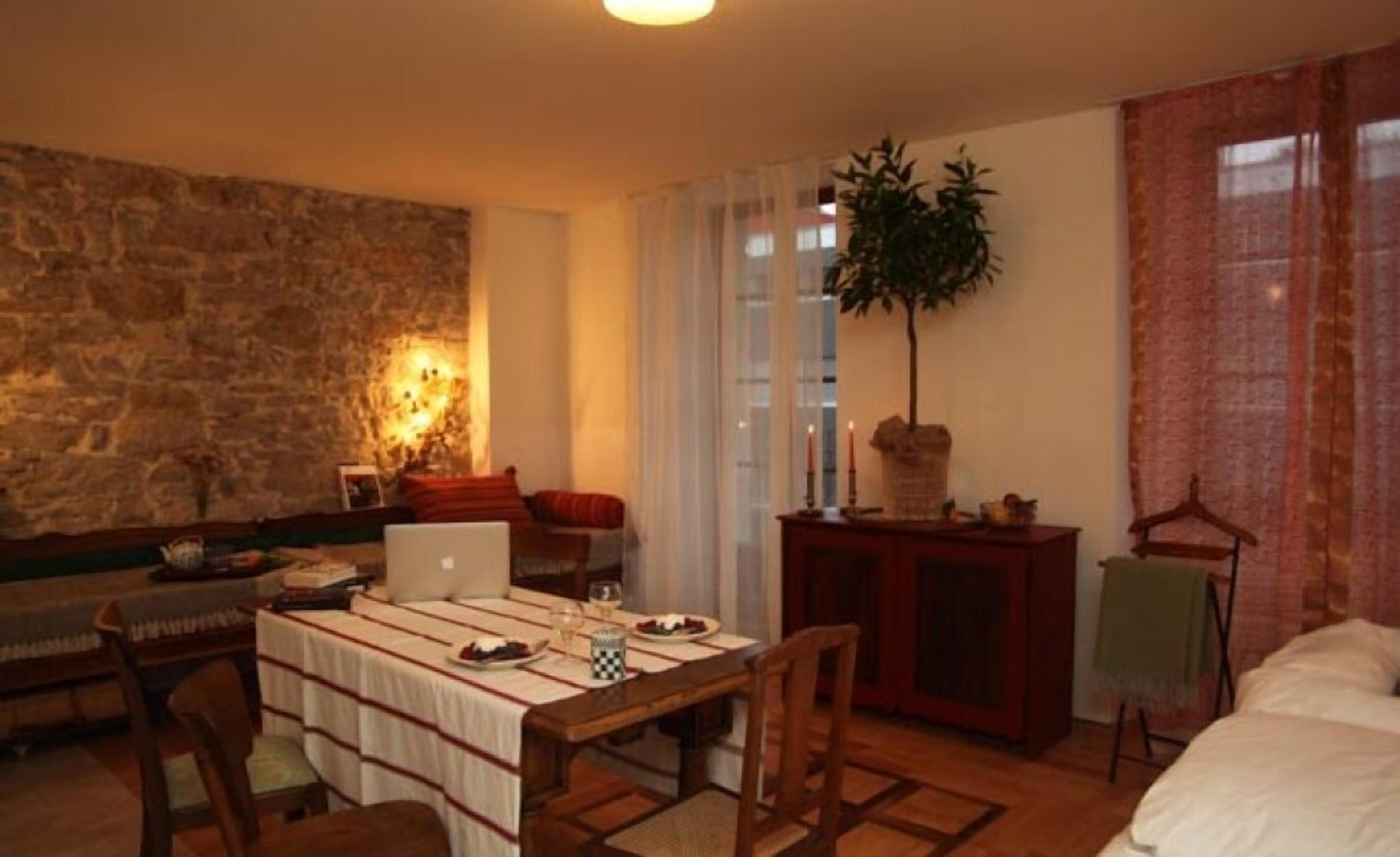 A cozy living room with a stone wall, a dining table set with plates and glasses, a laptop, and a plant.