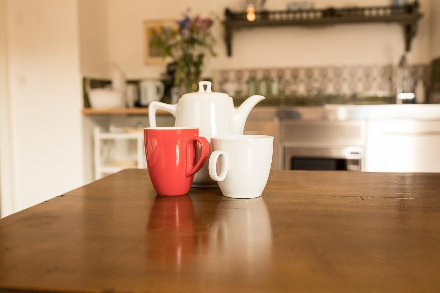 Une table en bois avec deux tasses, une rouge et une blanche, dans une cuisine.