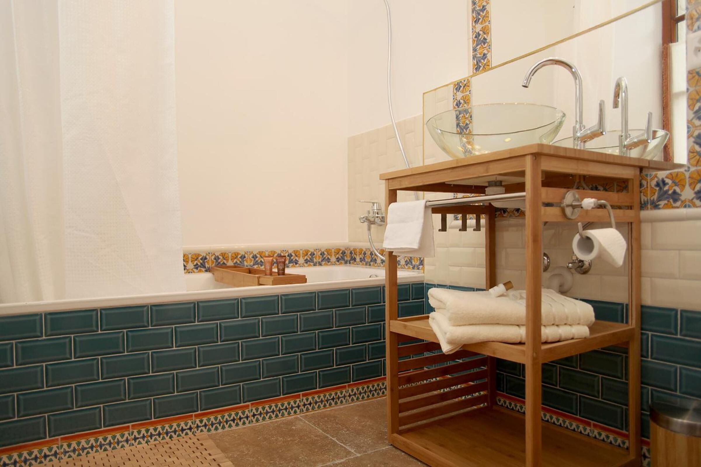 A bathroom with a glass basin sink, a wooden shelf with towels, and a tiled backsplash.