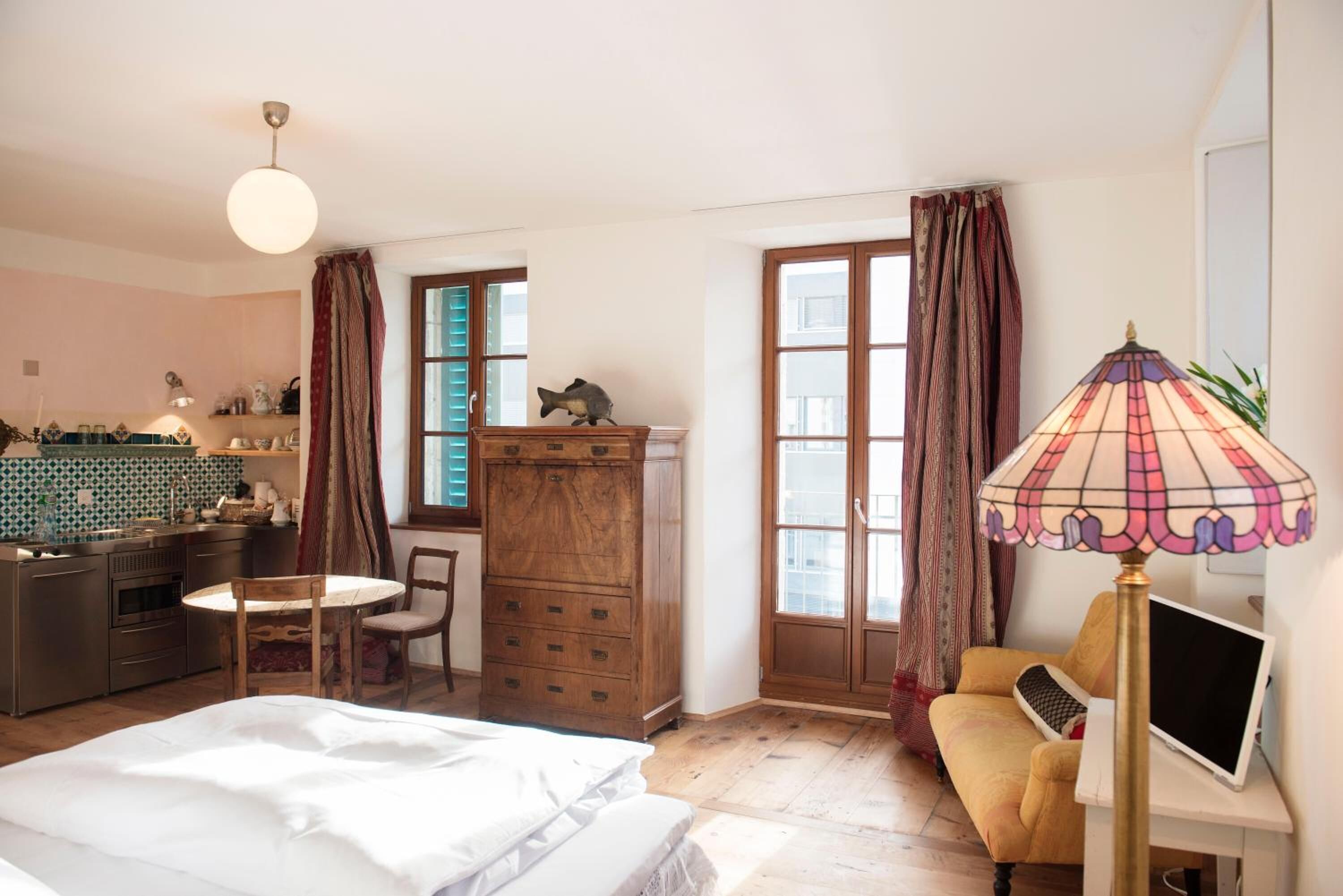 A bedroom with a bed, a desk with a computer, a chair, a dresser, and a window with curtains.
