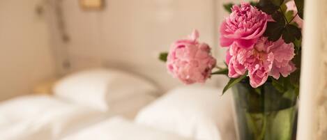 A bed with white linens and a vase with pink flowers on a bedside table.
