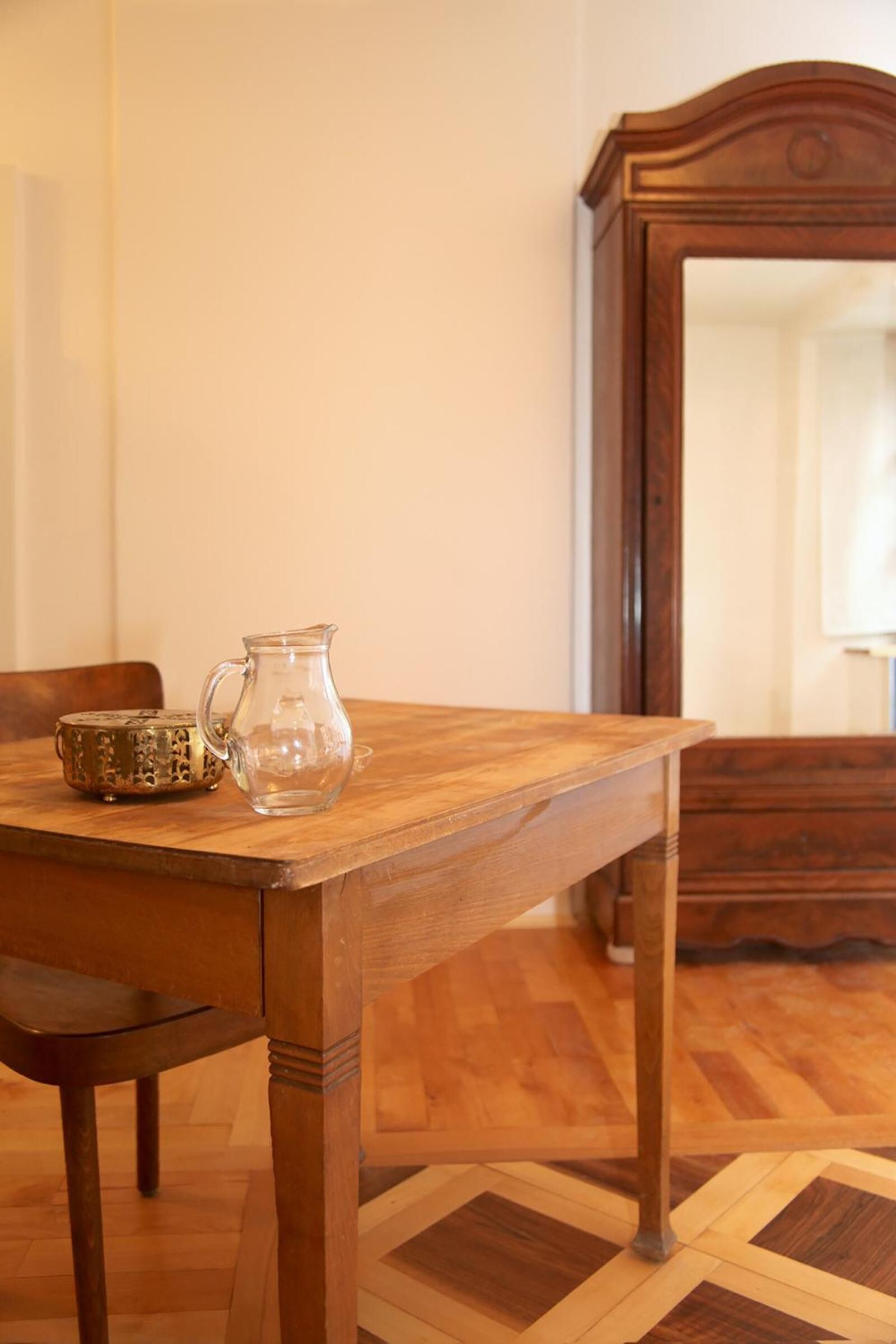 Una mesa de madera con una jarra transparente y un recipiente decorativo. Una silla está colocada frente a la mesa.