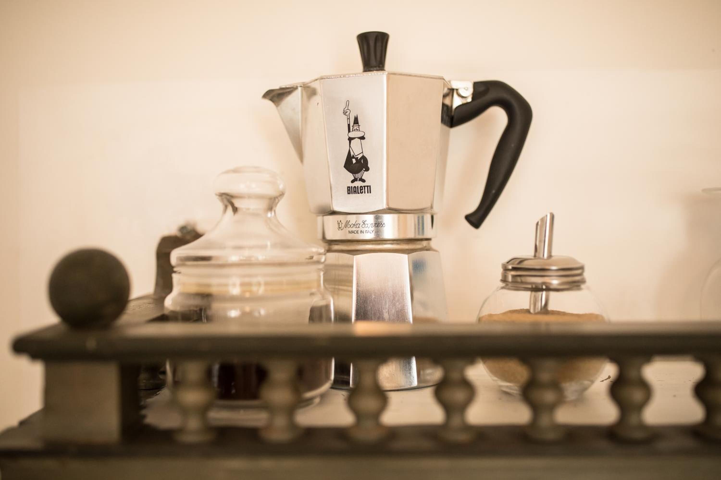 A coffee maker with a handle and spout, a glass jar, and a metal container on a table.