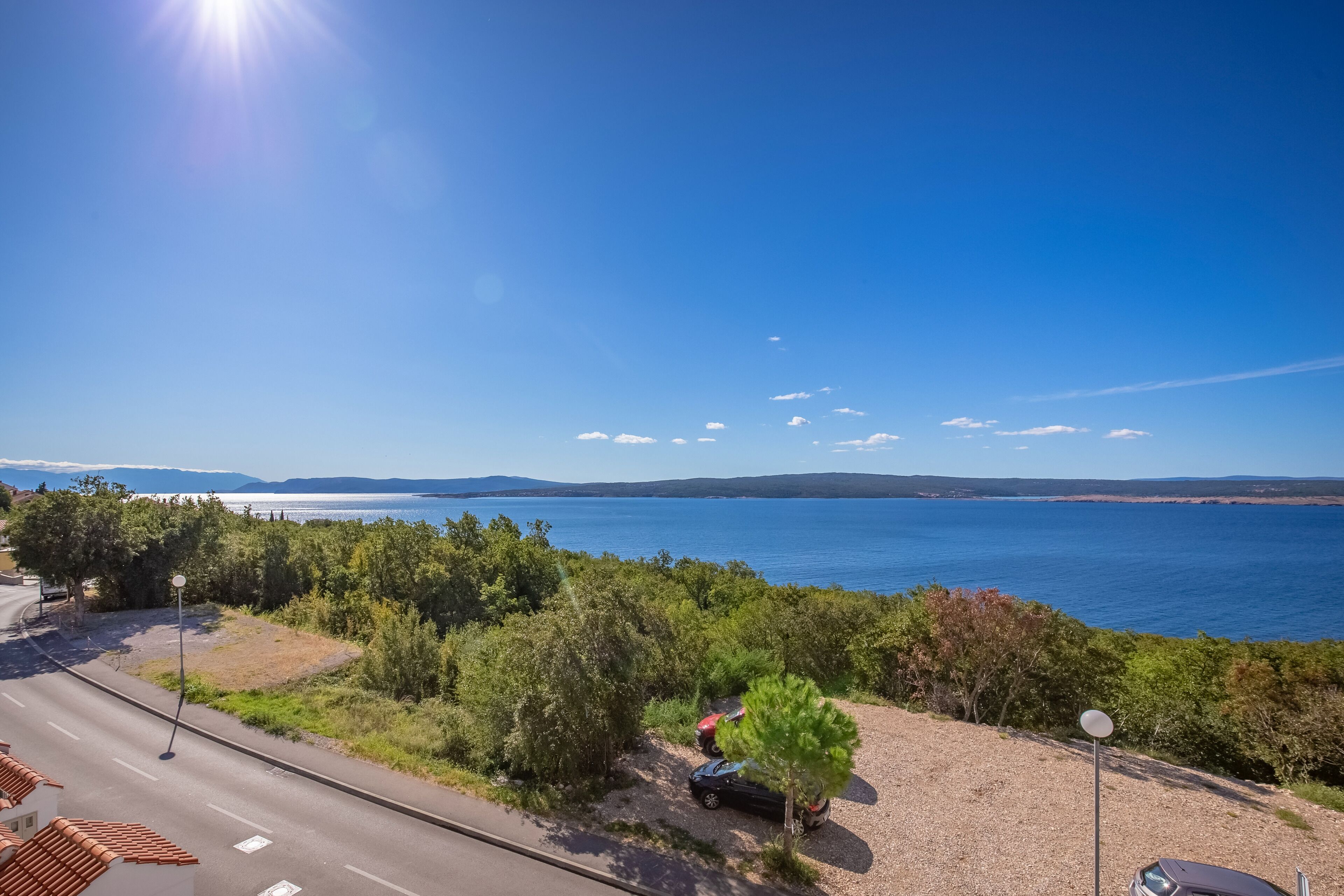 Une route côtière bordée de voitures garées, un ciel bleu dégagé et une vue sur la mer.