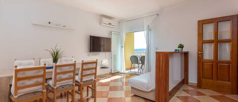 A room with a dining table, chairs, a sofa, a TV, and a door leading to an outdoor area.