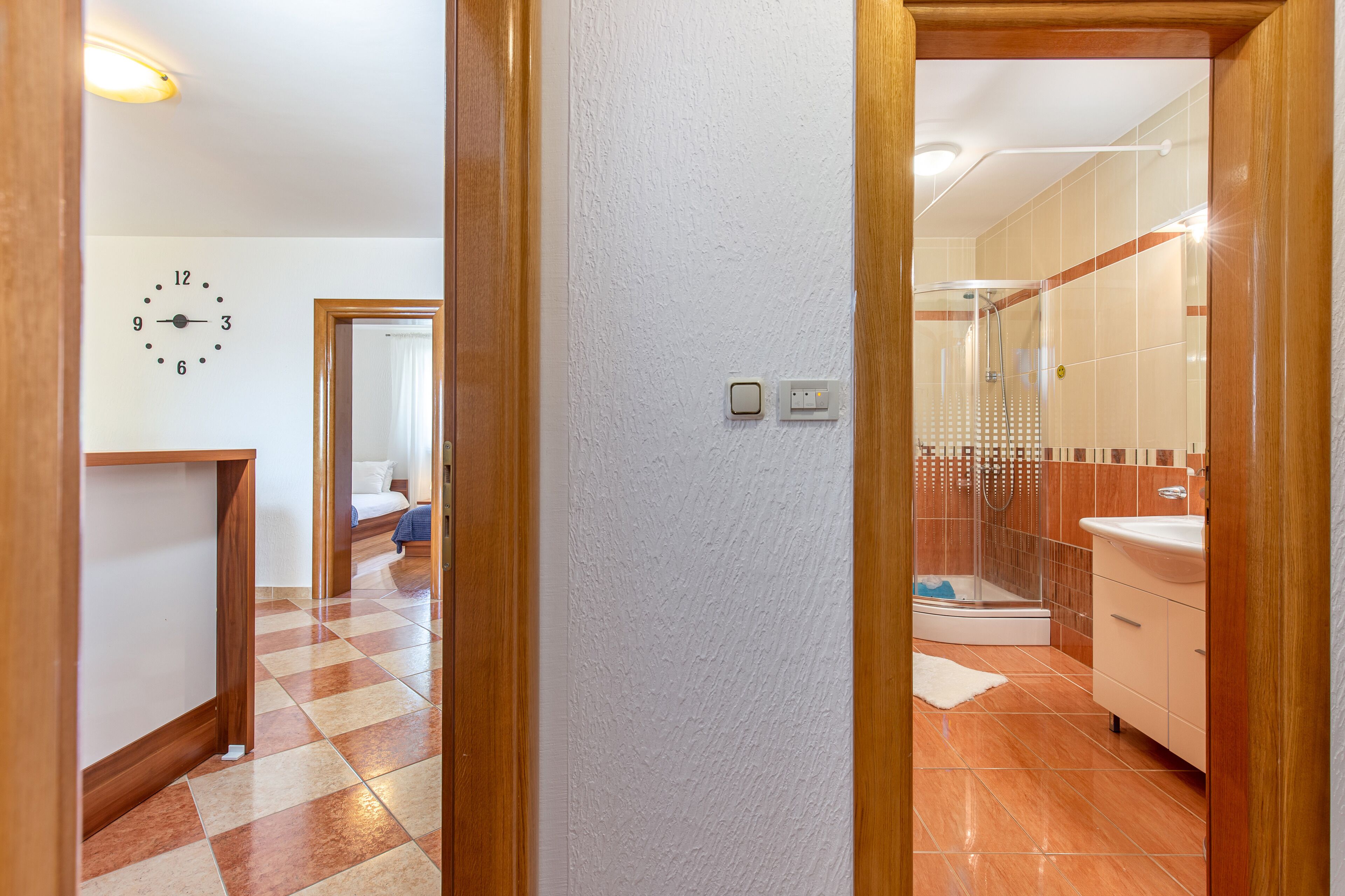 A hotel room with a checkered floor, a visible clock, a shower area, and a bathroom with a sink and mirror.