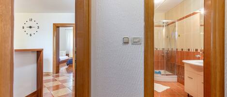 A hotel room with a checkered floor, a visible clock, a shower area, and a bathroom with a sink and mirror.