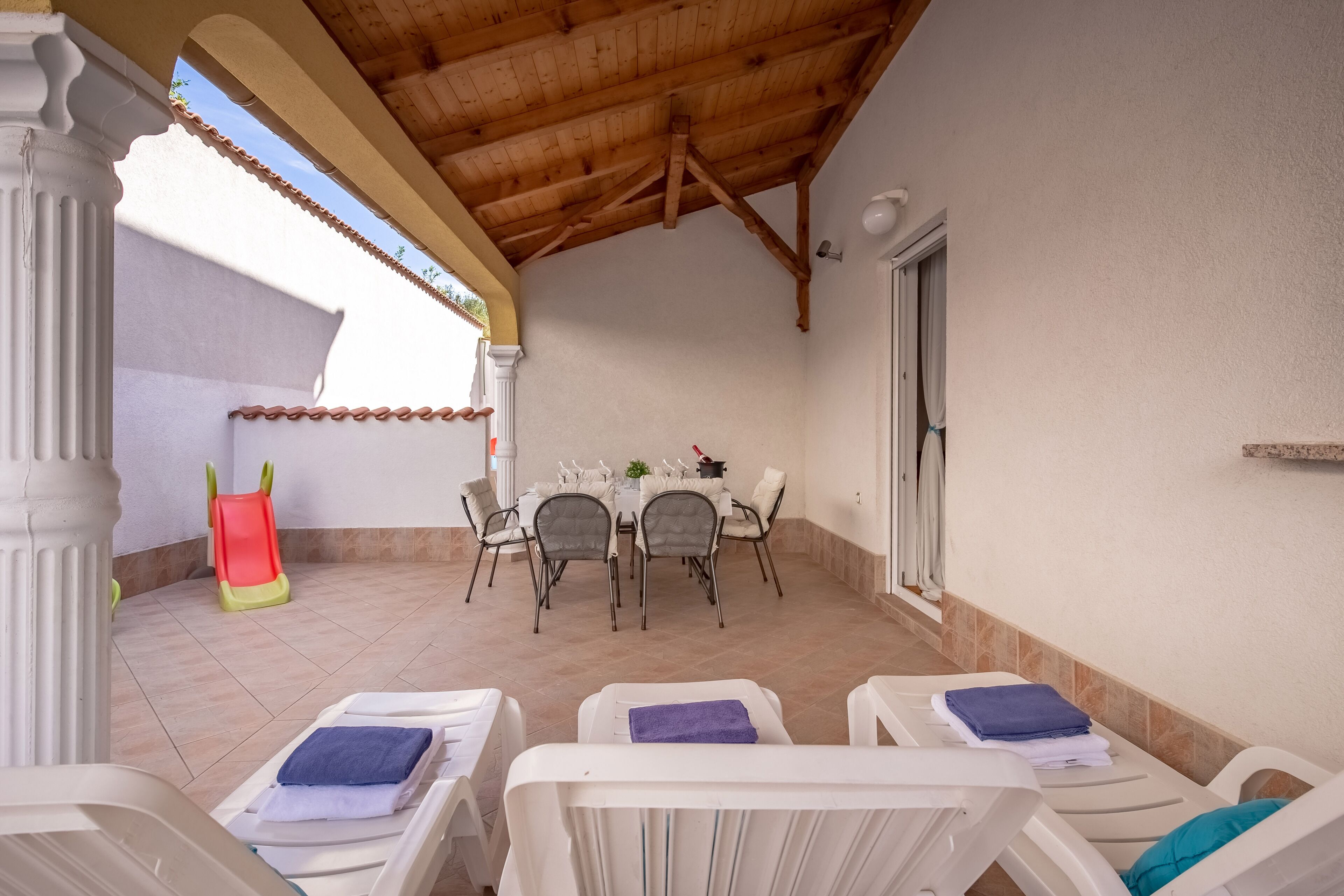 A covered patio with a dining area, chairs, and a slide.
