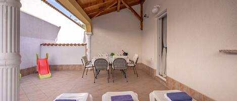 A covered patio with a dining area, chairs, and a slide.