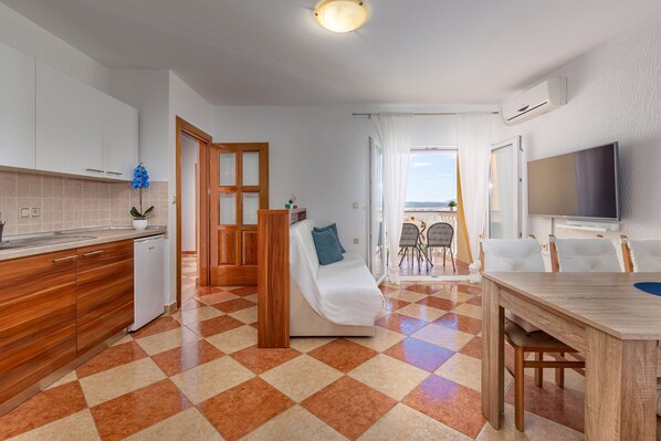 Uma cozinha moderna com lava-louças, uma área de refeições com mesa e cadeiras de madeira, um sofá com almofada azul e uma TV fixada na parede.