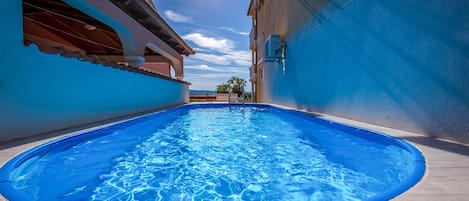 A swimming pool with a clear blue water surface, surrounded by a light-colored tiled deck.