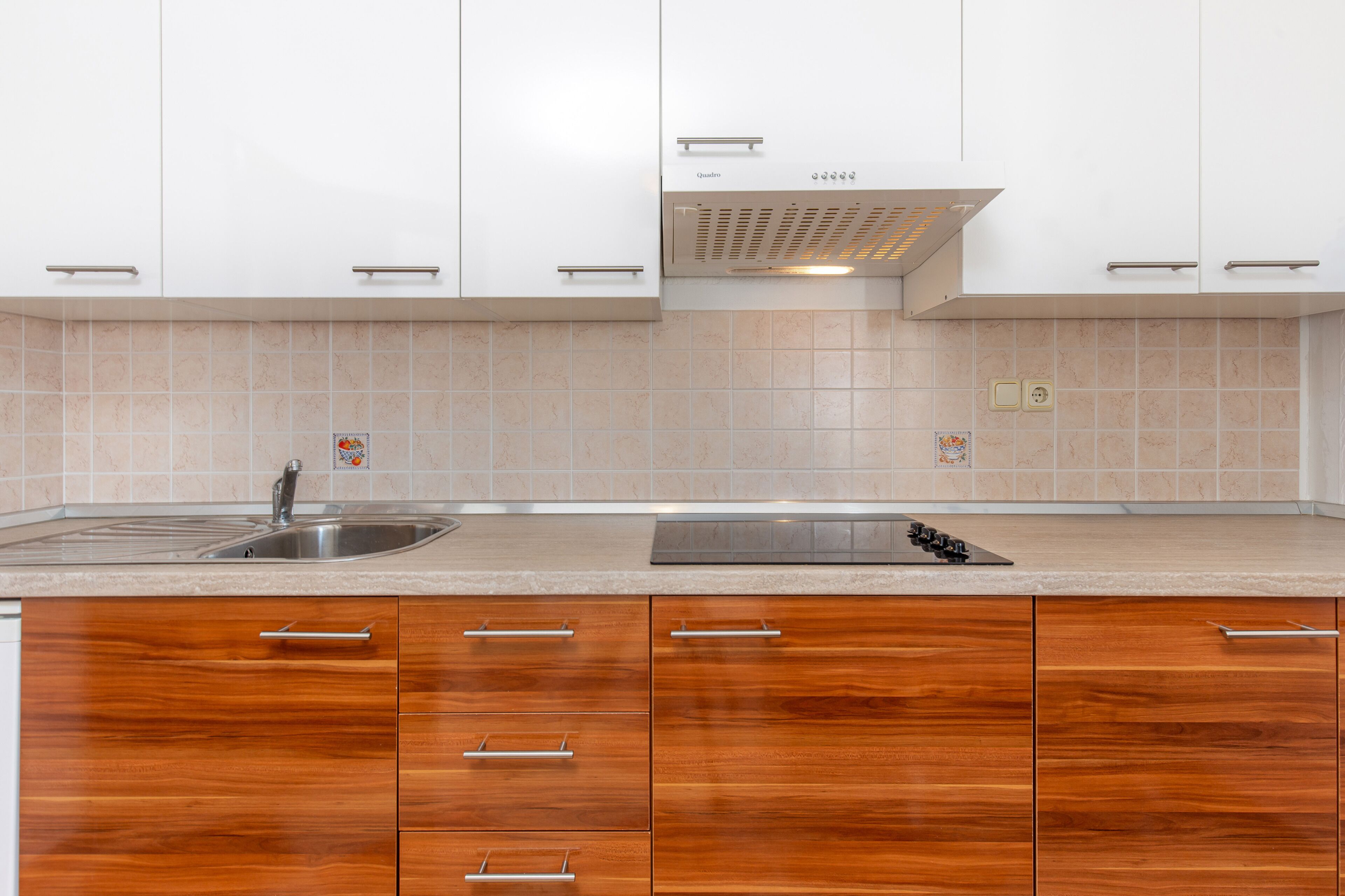 A modern kitchen with white cabinets, a stainless steel sink, and wooden drawers.